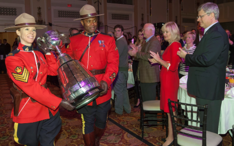 A male and a female RCMP officer carry the Grey Cup into a crowded room.